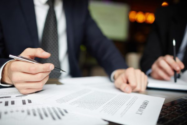 Closeup portrait of two unrecognizable business people wearing black formal suits signing contract papers at table during meeting